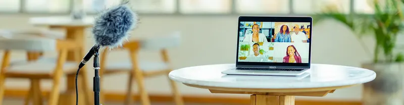 Podcast mikrofon és laptop egy kerek asztalon, a képernyőn online videóbeszélgetés