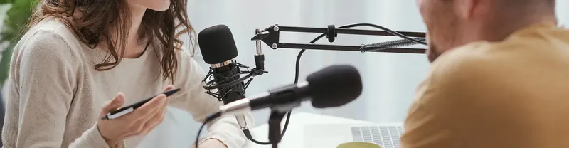 Okostelefont tartó nő podcast felvétel közben, előtte stúdiómikrofonok