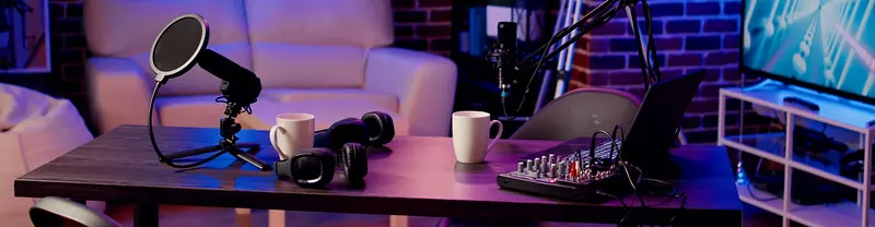 Podcast stúdió asztal mikrofonokkal, fejhallgatókkal, bögrékkel és keverőpulttal neonfényben