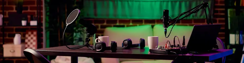 Podcast felvételi asztal mikrofonállvánnyal, laptoppal és keverőpulttal zöld fényben