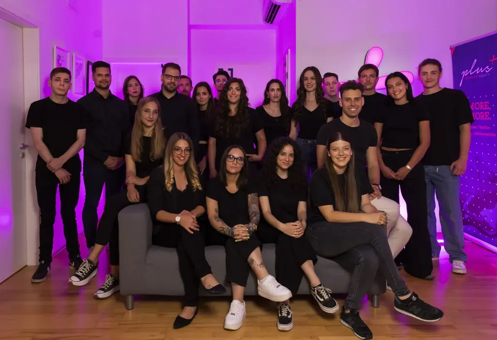 A Plus Creative Group csapata fekete pólóban, lila fényekkel megvilágított irodában